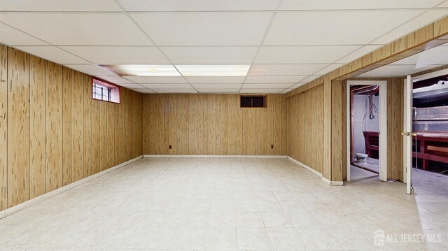 basement with wooden walls, a paneled ceiling, and baseboards