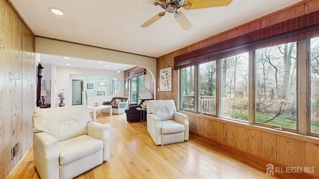 living area featuring arched walkways, light wood-style floors, wood walls, and ceiling fan