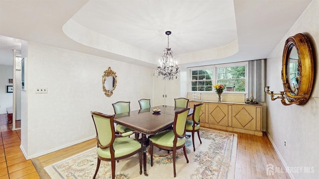 dining room with an inviting chandelier, a tray ceiling, light wood-style floors, and baseboards