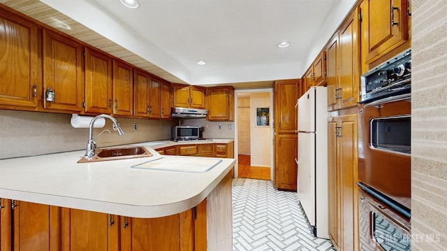 kitchen with light countertops, a sink, freestanding refrigerator, a peninsula, and brown cabinetry