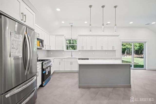 kitchen featuring sink, decorative light fixtures, vaulted ceiling, white cabinets, and appliances with stainless steel finishes