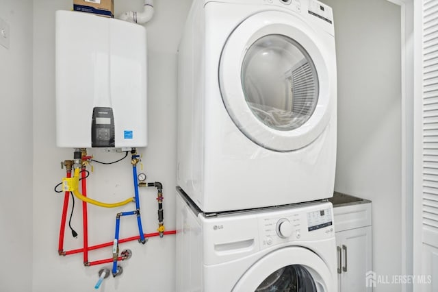 laundry room featuring stacked washing maching and dryer, cabinets, and tankless water heater