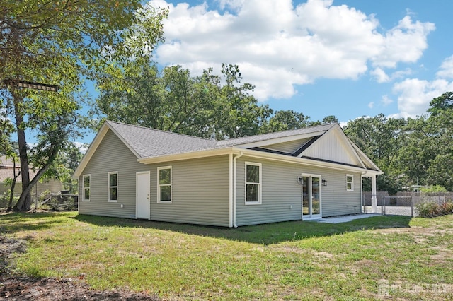 rear view of property with roof with shingles, fence, and a lawn