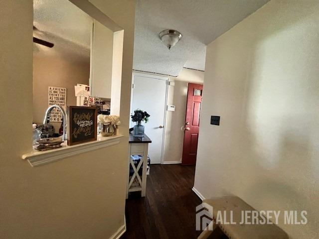 hallway featuring baseboards, a textured ceiling, and wood finished floors