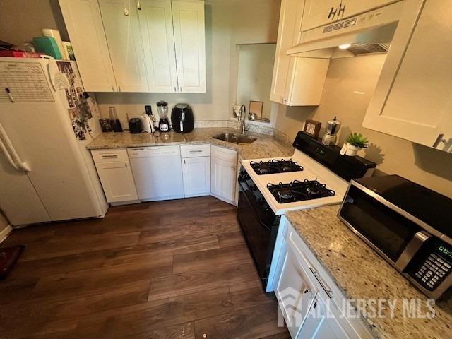 kitchen with under cabinet range hood, a sink, dark wood-style floors, white appliances, and white cabinets