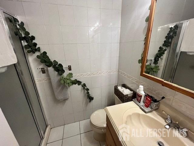 bathroom featuring toilet, vanity, a stall shower, tile patterned floors, and tile walls