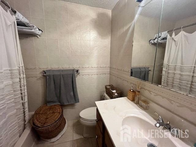 bathroom with tile patterned floors, toilet, a textured ceiling, tile walls, and vanity