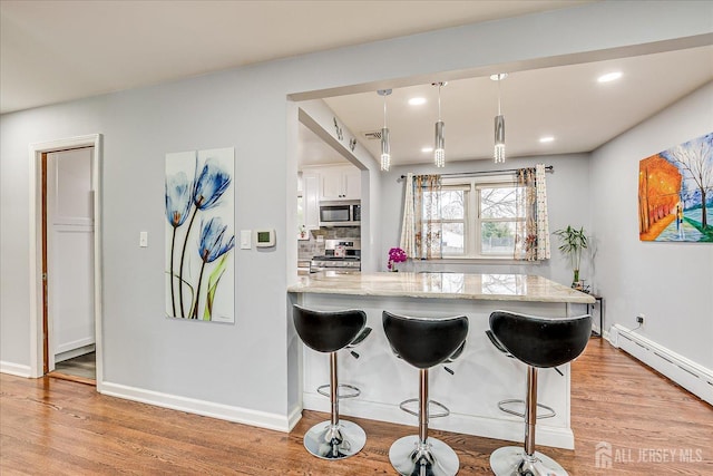 kitchen featuring a baseboard heating unit, light stone counters, appliances with stainless steel finishes, and light wood-style flooring