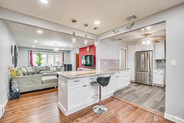 kitchen with visible vents, light wood-style flooring, open floor plan, freestanding refrigerator, and a peninsula