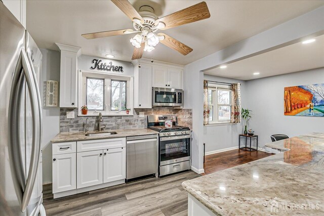 kitchen featuring tasteful backsplash, light wood-style flooring, appliances with stainless steel finishes, white cabinetry, and a sink