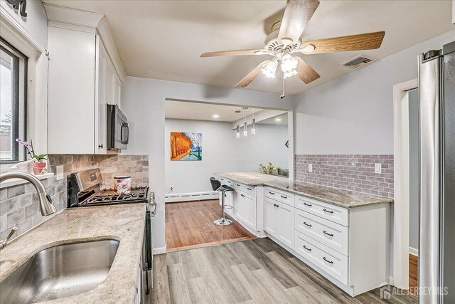 kitchen featuring visible vents, light wood-style flooring, baseboard heating, stainless steel appliances, and a sink