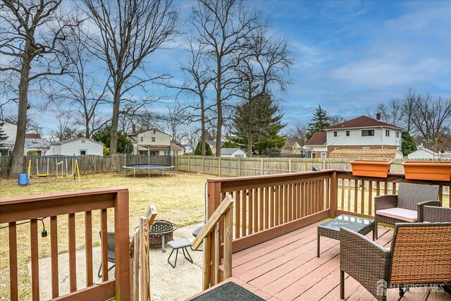 deck featuring a fire pit, a fenced backyard, a residential view, a trampoline, and a playground