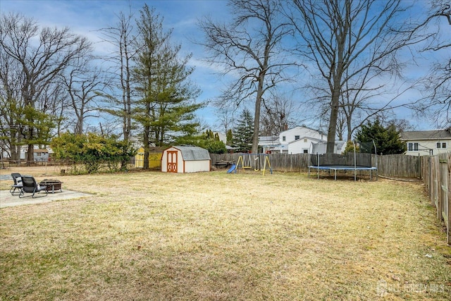 view of yard with an outdoor fire pit, a fenced backyard, a trampoline, an outdoor structure, and a playground