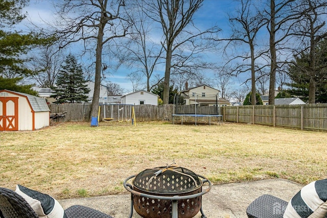 view of yard featuring an outdoor fire pit, a fenced backyard, an outbuilding, a trampoline, and a shed