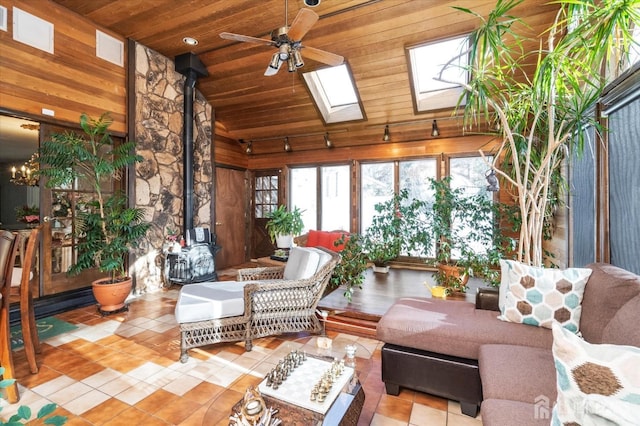 sunroom featuring ceiling fan with notable chandelier, wooden ceiling, vaulted ceiling with skylight, and a wood stove