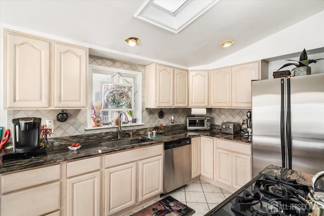 kitchen with sink, vaulted ceiling, light tile patterned floors, dark stone countertops, and appliances with stainless steel finishes