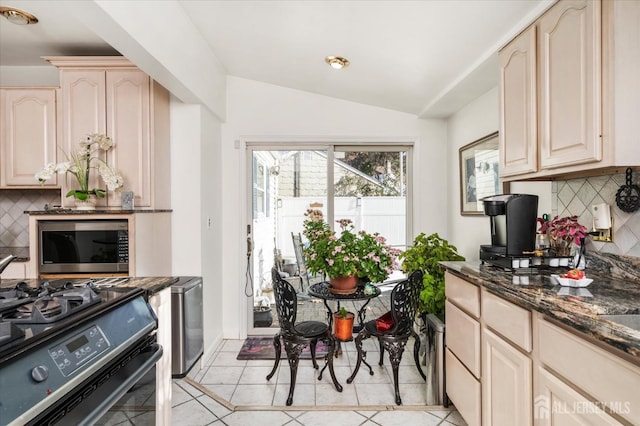 kitchen featuring lofted ceiling, tasteful backsplash, black gas range oven, light tile patterned floors, and dark stone countertops