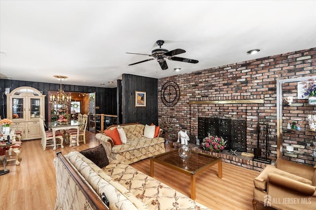 living room featuring wooden walls, ceiling fan with notable chandelier, a fireplace, and light hardwood / wood-style flooring