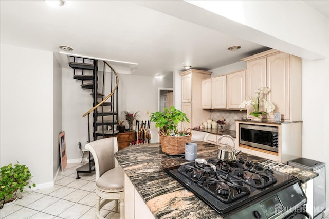 kitchen with dark stone countertops, stainless steel microwave, tasteful backsplash, light tile patterned flooring, and black gas stovetop