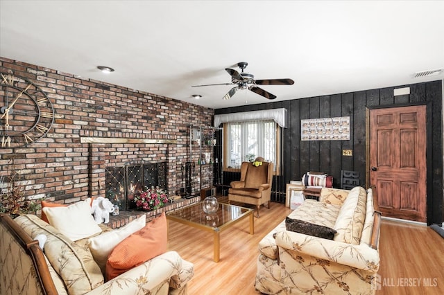 living room featuring hardwood / wood-style floors, a fireplace, ceiling fan, and brick wall