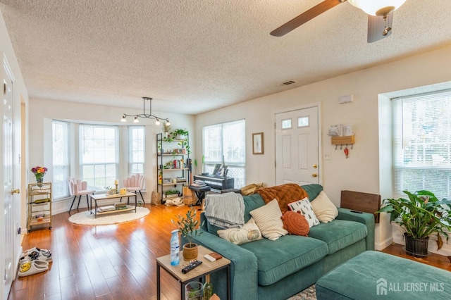 living area with a ceiling fan, a textured ceiling, visible vents, and wood finished floors