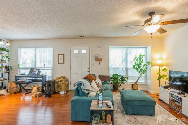 living room featuring ceiling fan, a textured ceiling, wood finished floors, and a healthy amount of sunlight