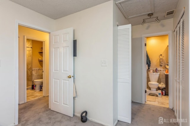 carpeted bedroom with attic access, connected bathroom, a closet, and a textured ceiling