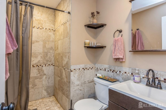 full bath featuring vanity, a tile shower, toilet, and tile walls