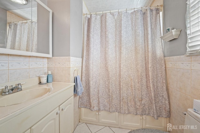 full bath with toilet, tile walls, tile patterned flooring, wainscoting, and vanity