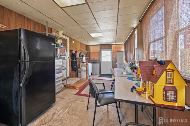 kitchen with freestanding refrigerator, wooden walls, brown cabinetry, and washer and dryer