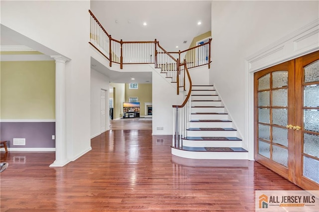 foyer featuring french doors, wood finished floors, stairs, a high ceiling, and ornate columns