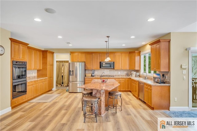 kitchen featuring appliances with stainless steel finishes, a sink, light wood-style flooring, a kitchen breakfast bar, and decorative backsplash