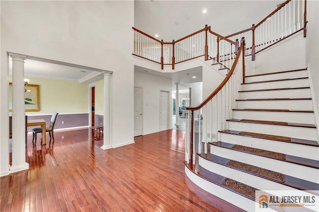 foyer featuring ornate columns, hardwood / wood-style flooring, a towering ceiling, stairs, and ornamental molding