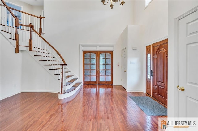entrance foyer featuring french doors, a towering ceiling, stairs, healthy amount of natural light, and wood-type flooring