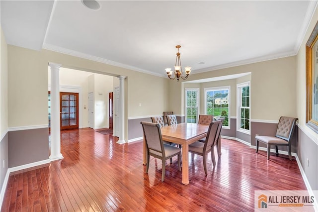 dining room featuring ornate columns, a chandelier, hardwood / wood-style flooring, baseboards, and crown molding