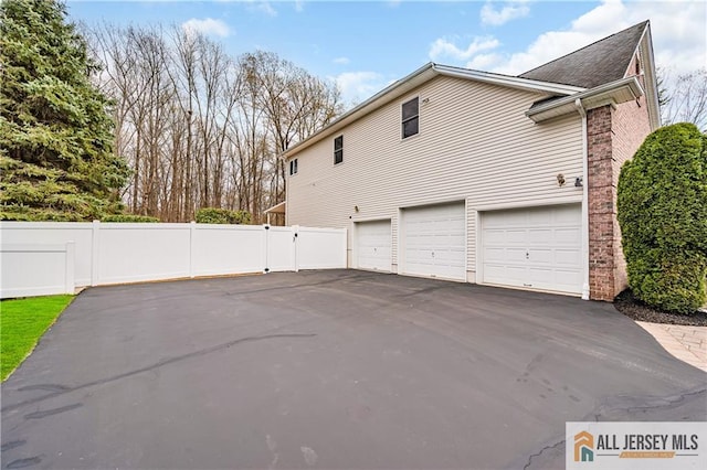 view of home's exterior with an attached garage, driveway, fence, and roof with shingles