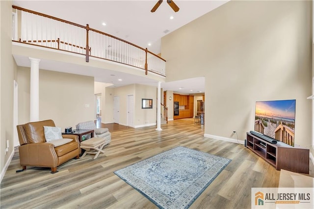living room with ceiling fan, a high ceiling, wood finished floors, decorative columns, and baseboards