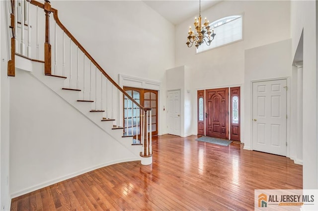 entryway with healthy amount of natural light, wood-type flooring, a chandelier, stairs, and a towering ceiling
