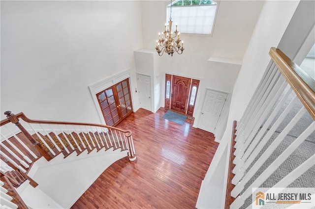 entryway featuring stairs, a towering ceiling, wood finished floors, and a chandelier