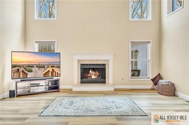 unfurnished living room featuring wood finished floors, a towering ceiling, a lit fireplace, and plenty of natural light