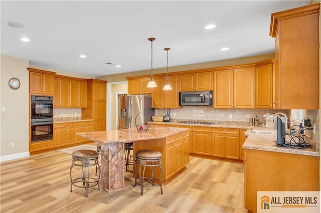 kitchen with appliances with stainless steel finishes, light wood-type flooring, a sink, light stone counters, and tasteful backsplash