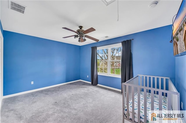unfurnished bedroom featuring carpet floors, baseboards, attic access, ceiling fan, and a crib