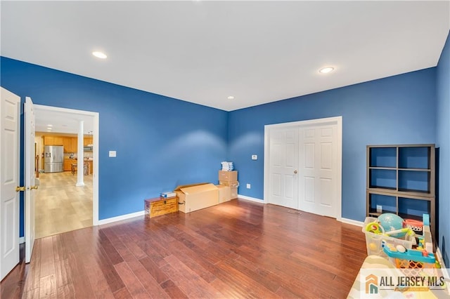 unfurnished bedroom with stainless steel fridge with ice dispenser, wood finished floors, baseboards, and recessed lighting