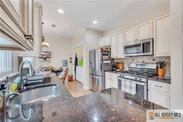 kitchen featuring appliances with stainless steel finishes, separate washer and dryer, a sink, backsplash, and dark stone countertops