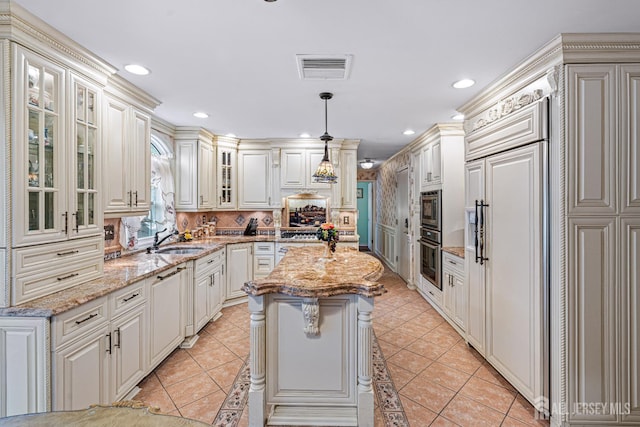 kitchen with a sink, built in appliances, a center island, backsplash, and glass insert cabinets