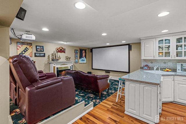 cinema room with a sink, light wood-style flooring, recessed lighting, and a warm lit fireplace