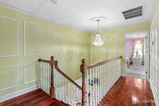 hall with an upstairs landing, hardwood / wood-style floors, a decorative wall, and a chandelier