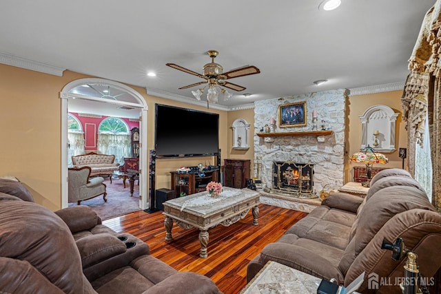 living area featuring ceiling fan, ornamental molding, a stone fireplace, wood-type flooring, and recessed lighting