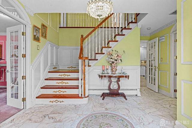 staircase featuring a decorative wall, french doors, a chandelier, wainscoting, and marble finish flooring