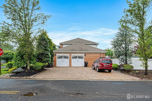 view of front of property with fence, roof with shingles, driveway, brick siding, and a garage